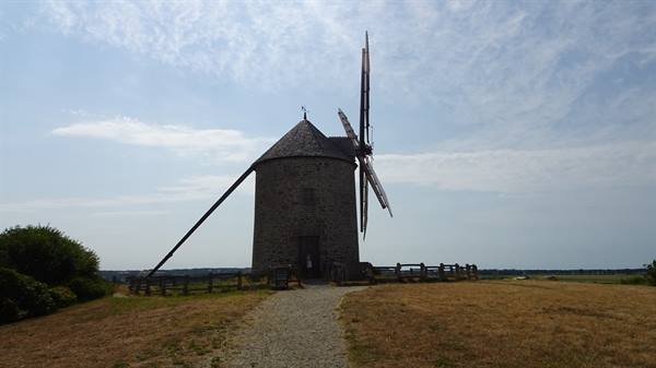 Old stone windmill with wooden sails, gravel path across open fields