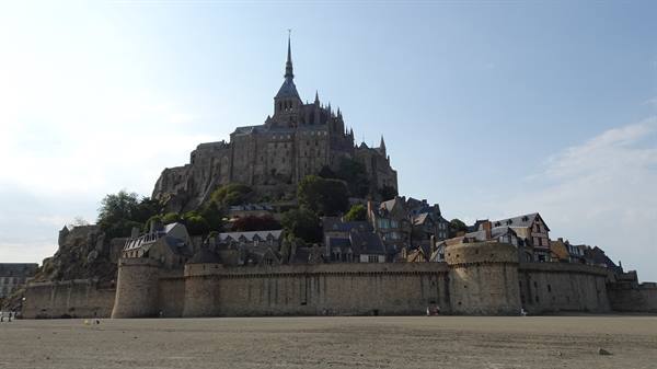 Mont Saint Michel: stone abbey and ramparts on the island, sand and pale sky