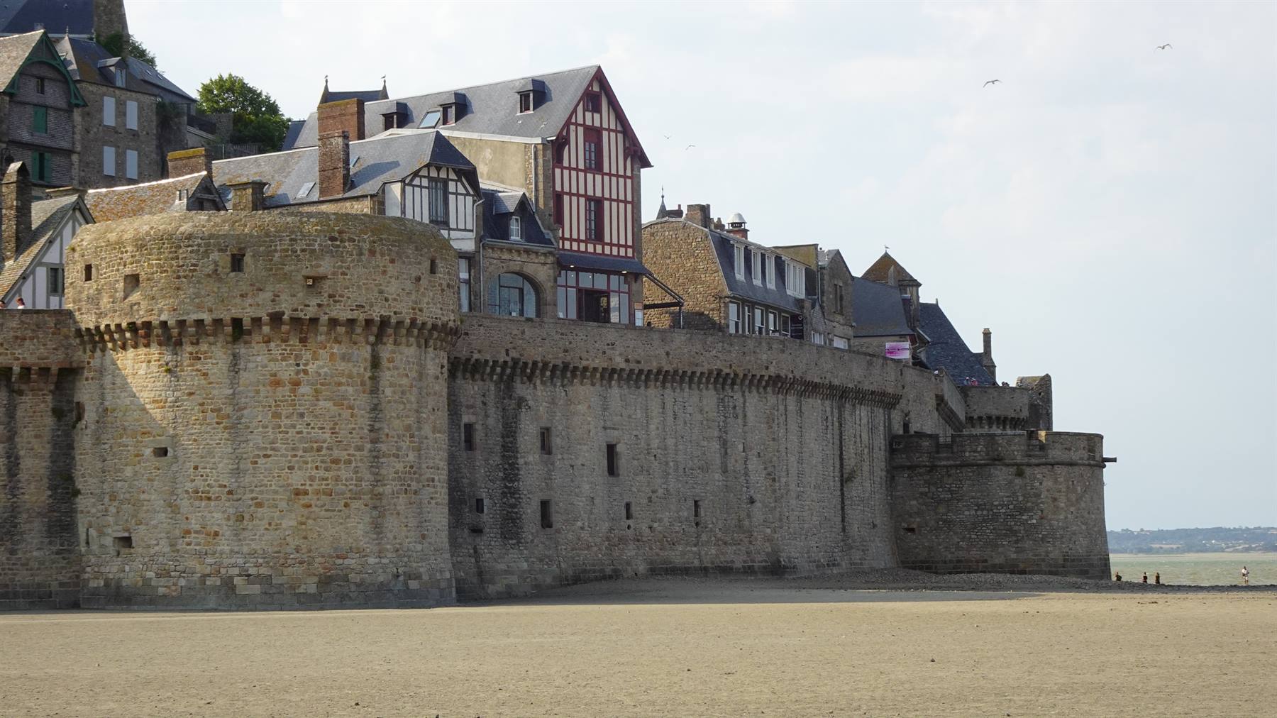 Mura fortificate in pietra e case a graticcio, sabbia in primo piano, Mont Saint Michel