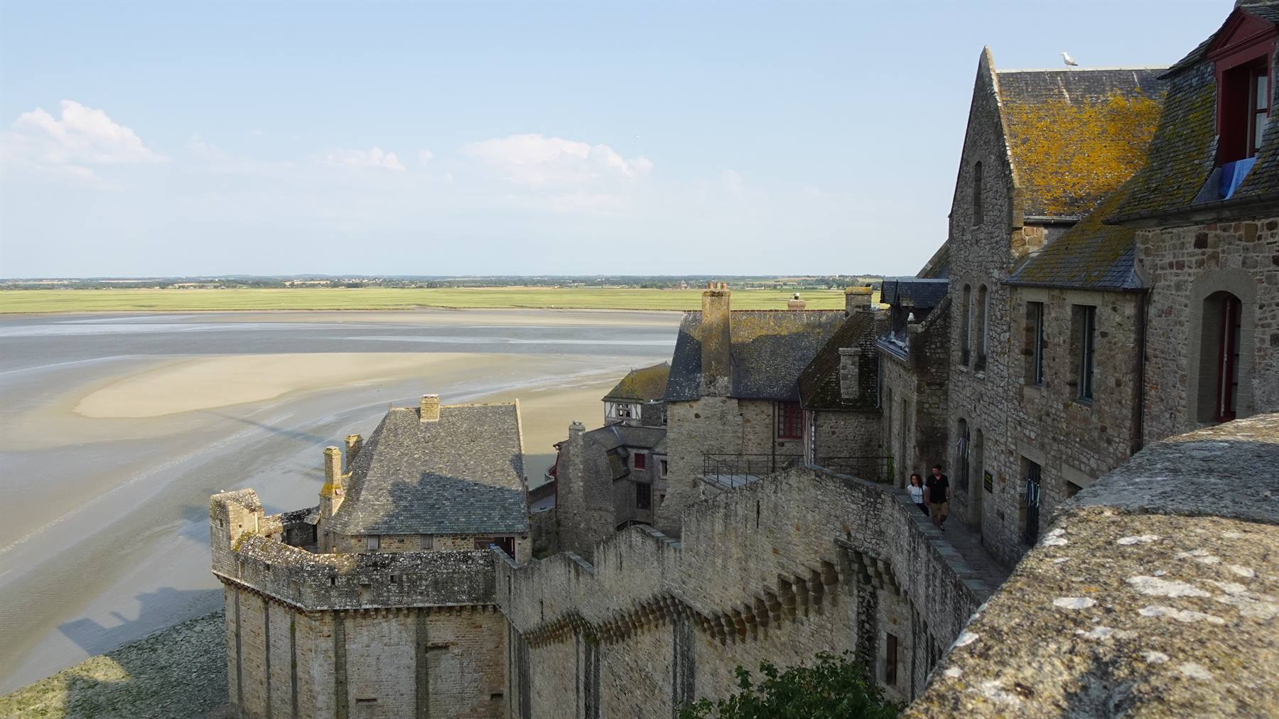 Mura di pietra di Mont Saint Michel sulla baia sabbiosa in luce diurna