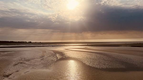 Low tide at Gouville sur Mer, sunlight breaking through clouds over the bay