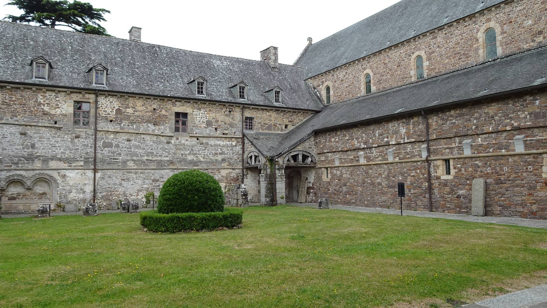 Chiostro dell'abbazia di La Lucerne, muri di pietra, prato e cielo grigio
