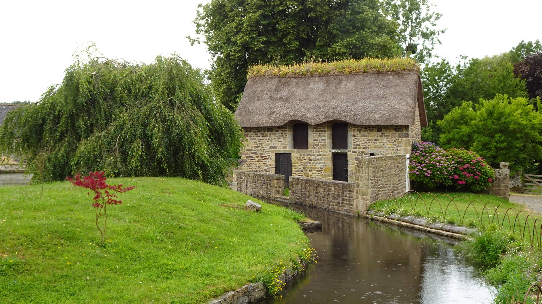 Saint-Céneri-le-Gérei, vecchio edificio in pietra con tetto di paglia lungo il fiume