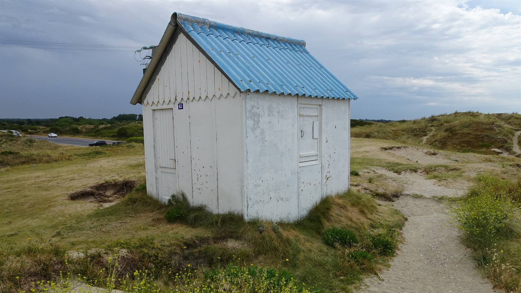 Capanella di legno bianco con tetto azzurro tra le dune erbose di Gouville sur Mer