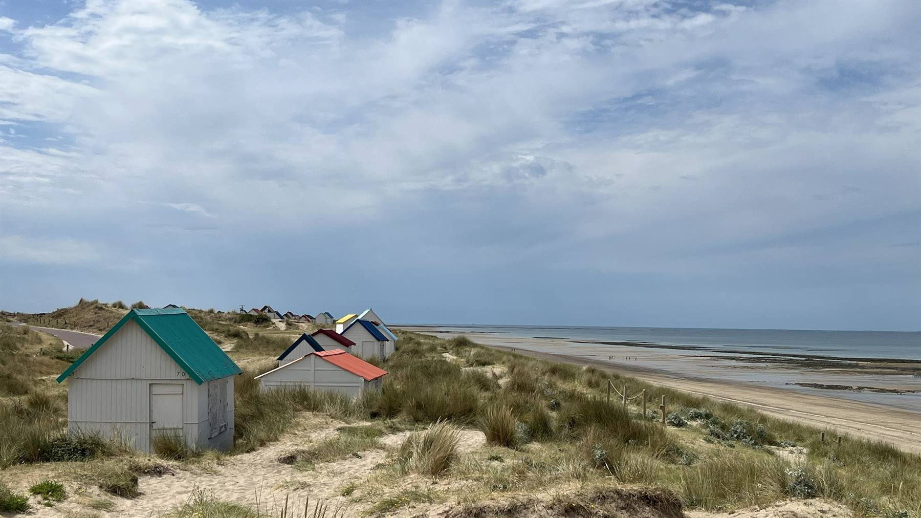 Capanne colorate tra le dune erbosa di Gouville sur Mer, spiaggia bassa sotto nuvole