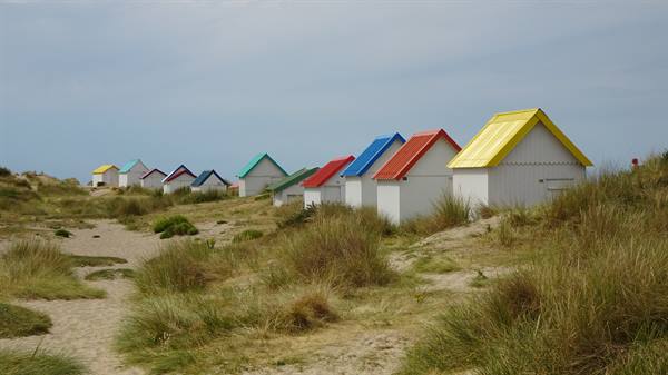 White beach huts with colorful roofs among grassy dunes in Gouville sur Mere