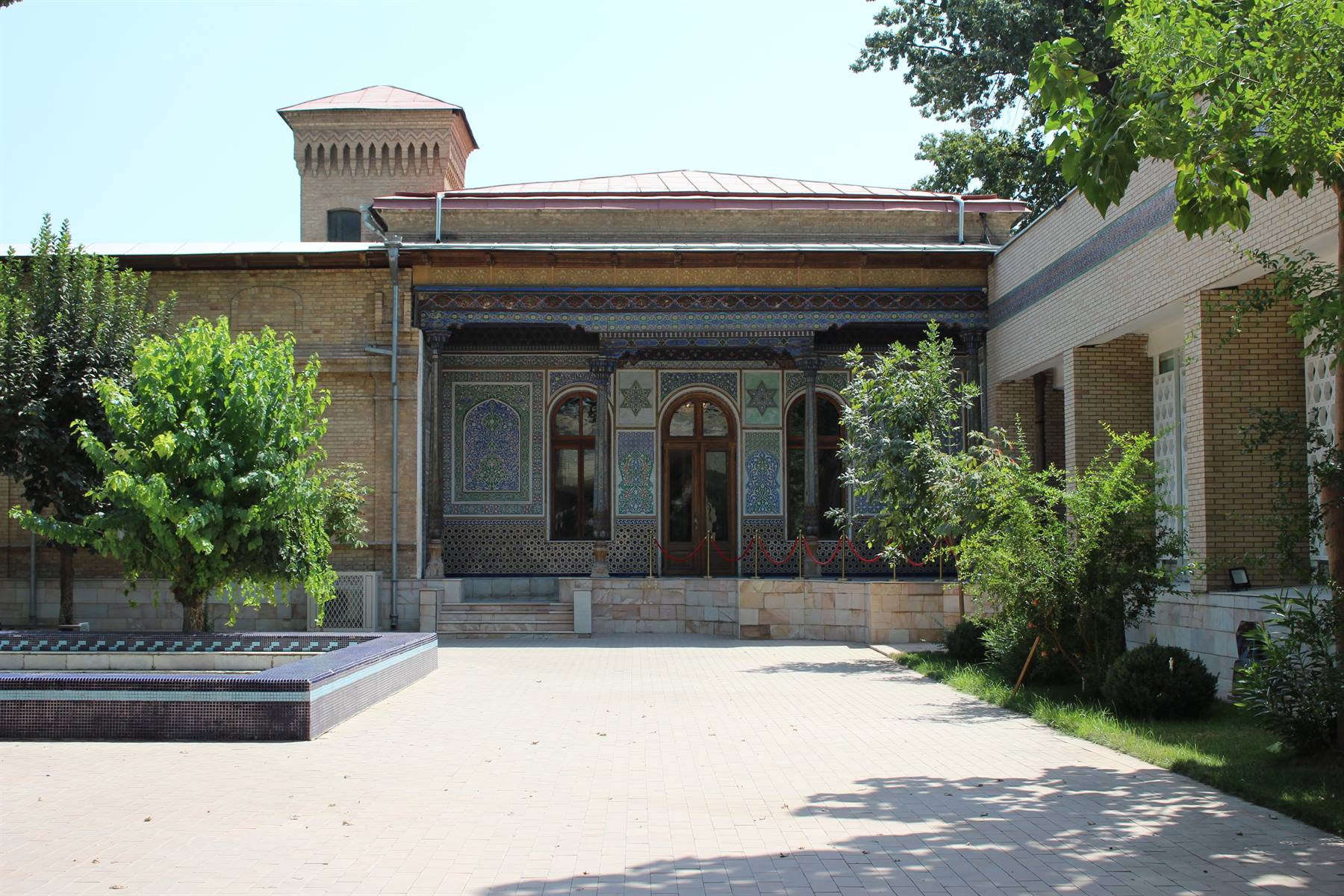 Palazzo in mattoni decorati con maioliche blu nel cortile ombreggiato di Tashkent