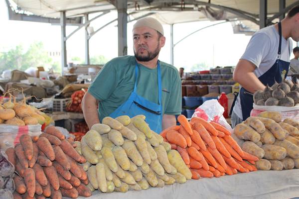 Mercato di Tashkent, venditore tra mucchi di carote e patate