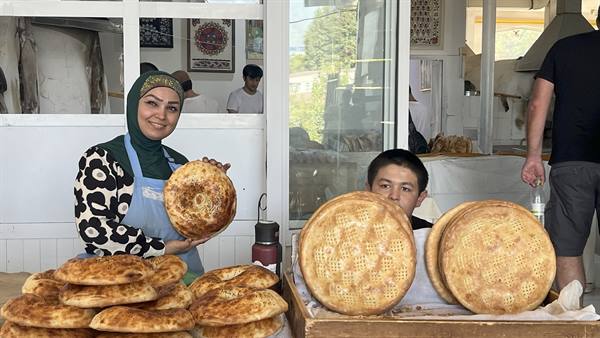 Donna velata mostra il pane tandoor accanto a un bambino, bancarella di lepyoshka