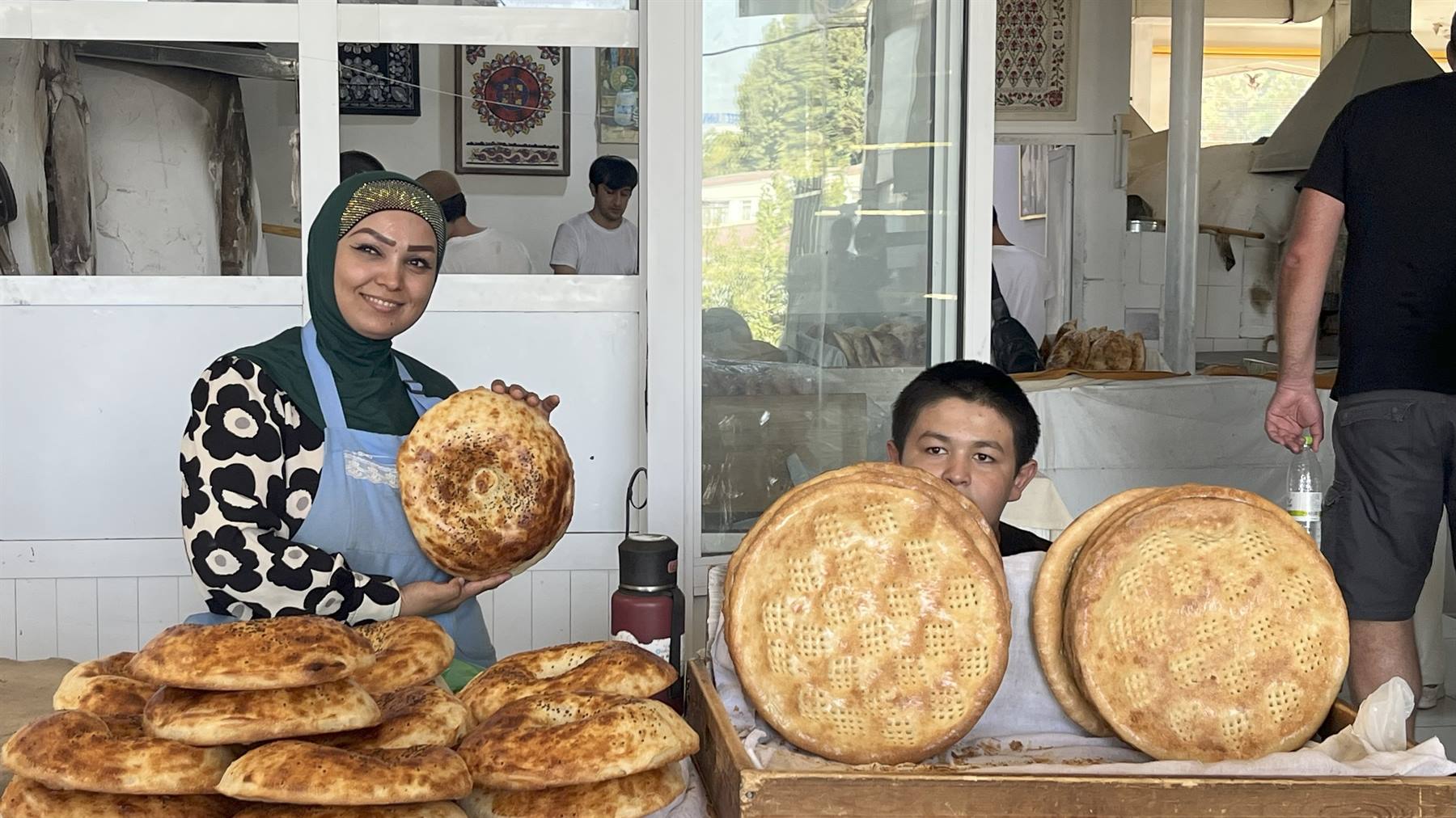 Donna velata mostra il pane tandoor accanto a un bambino, bancarella di lepyoshka
