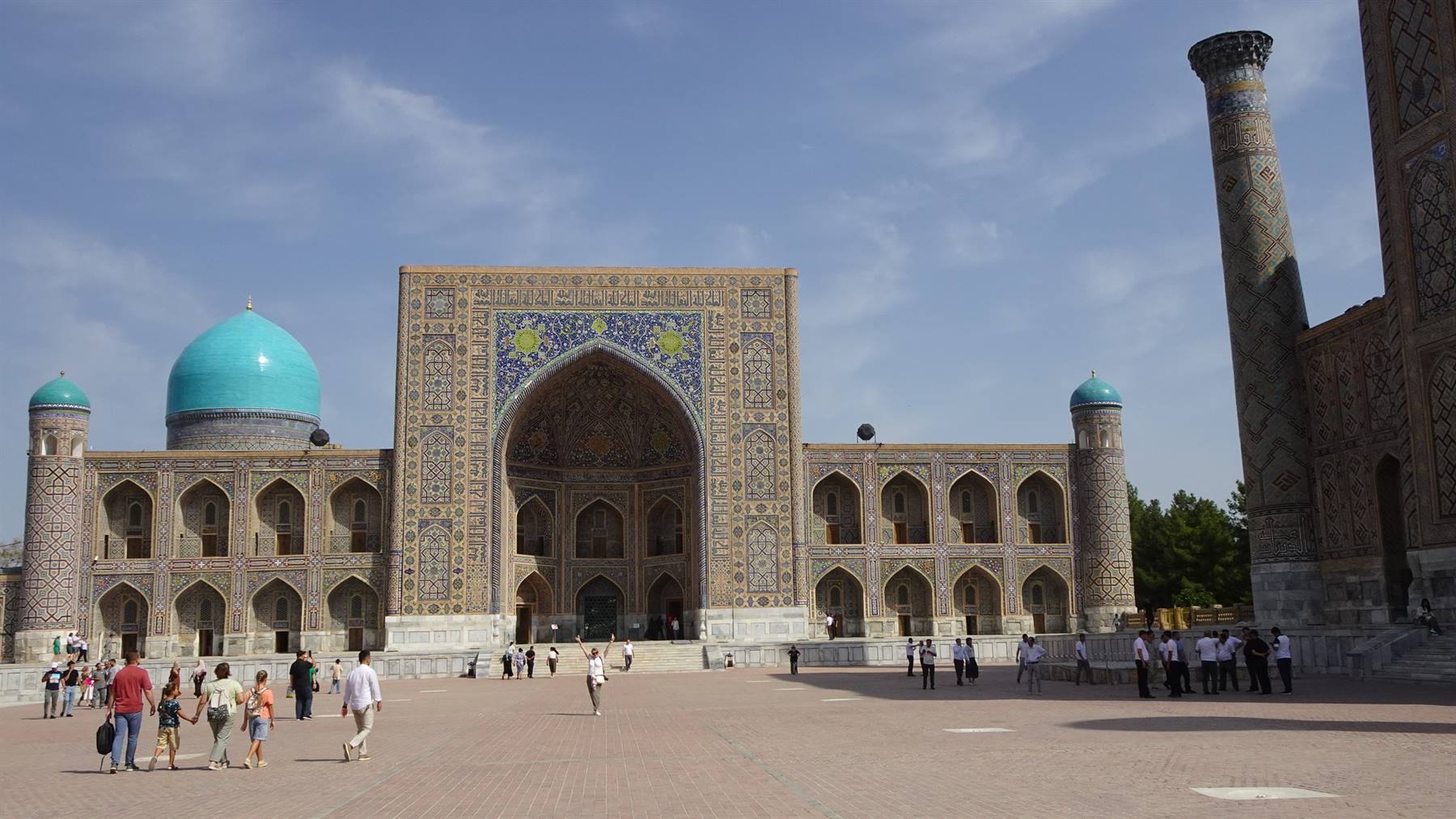 Turisti passeggiano davanti al madrasa di maioliche azzurre nella piazza Registan di Samarcanda