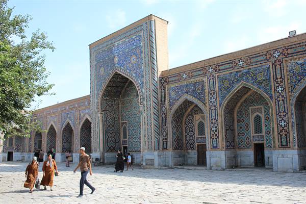 Visitatori camminano davanti alle maioliche azzurre del Registan, Samarcanda