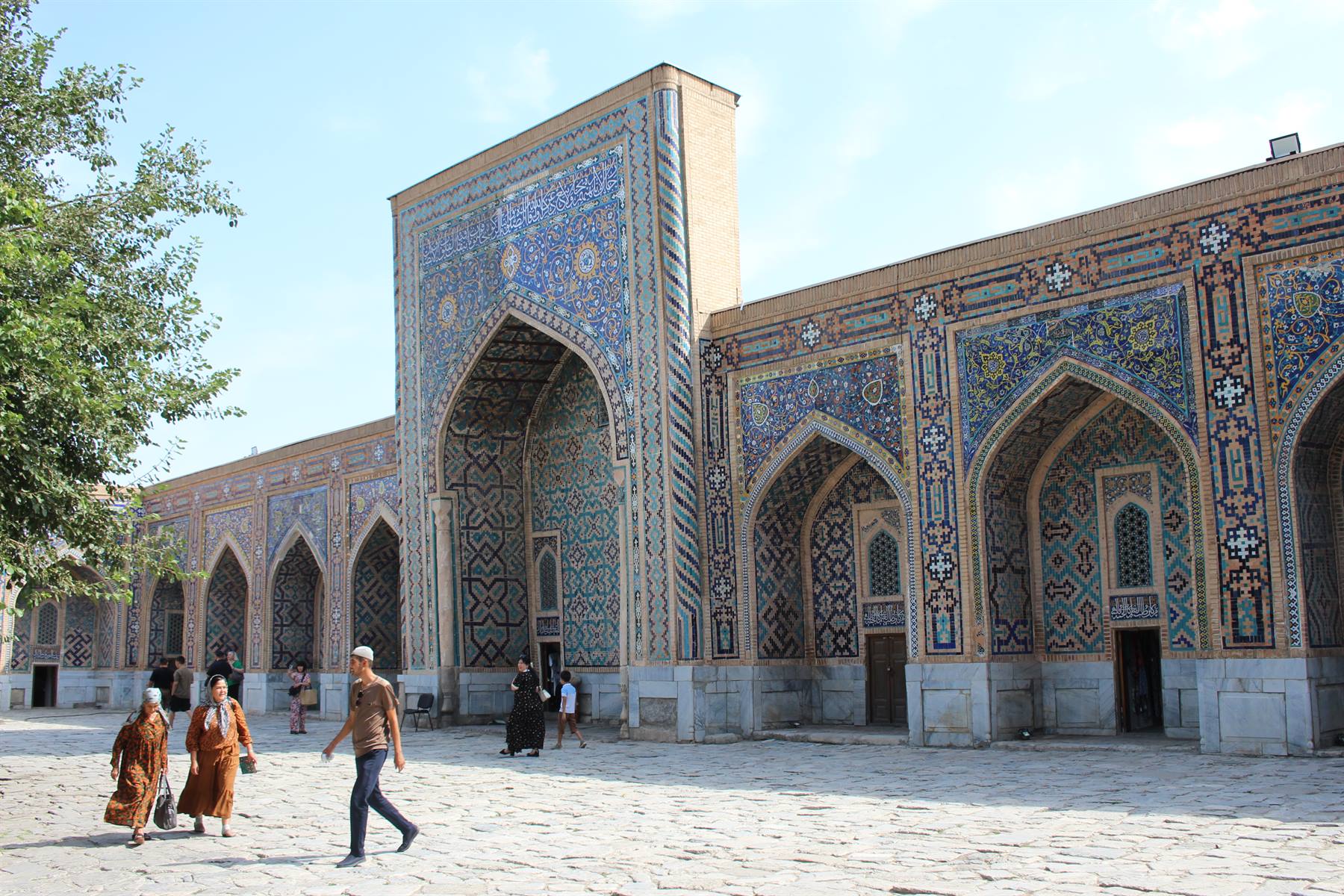 Visitatori camminano davanti alle maioliche azzurre del Registan, Samarcanda