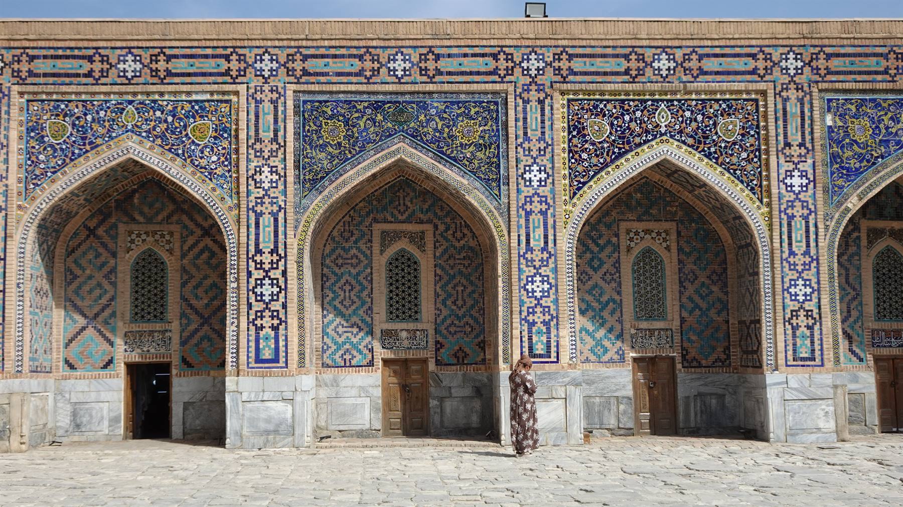 Donna cammina davanti alla facciata maiolicata del Registan a Samarcanda