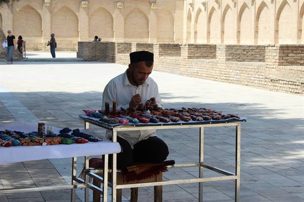 Venditore di calzature ricamate davanti ai portici di mattoni di Bukhara