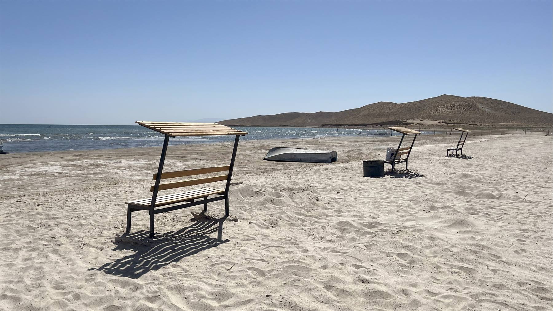 Panchine in legno con tettoia sulla sabbia, barca rovesciata, Aydar Lake