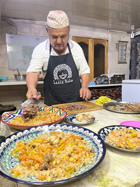 Lo chef mette la carne sul plov nei piatti ceramici decorati, cucina di Tashkent