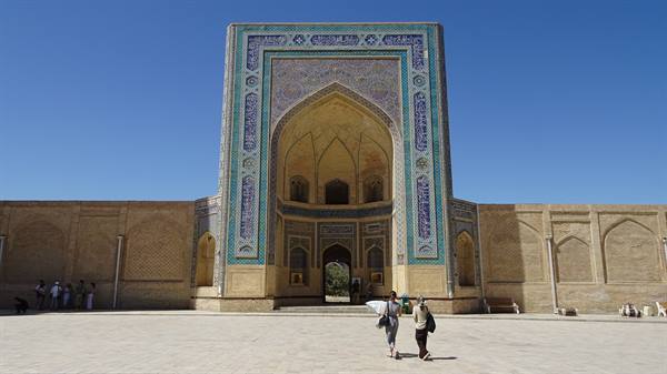 Portale in maiolica blu di una madrasa di Bukhara, due turiste camminano nella piazza