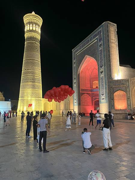 Bukhara, notte: turisti con palloncini rossi accanto al minareto illuminato