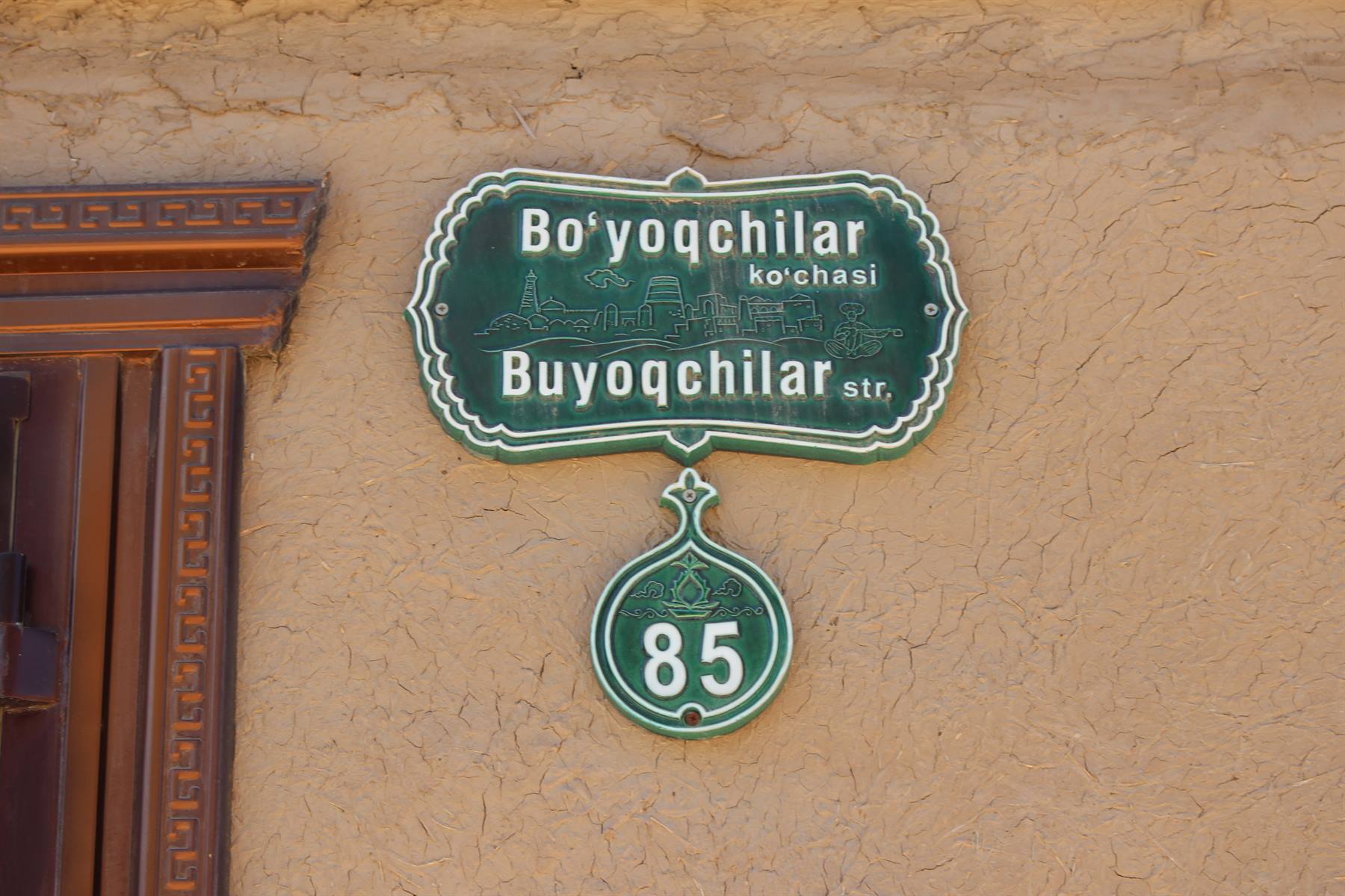 Insegna verde della via Bo'yoqchilar con numero civico 85 su muro crudo