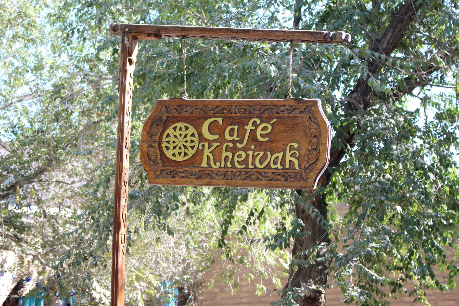 Insegna di legno intagliato del Café Kheivak tra gli alberi di Bukhara