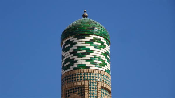 Minareto decorato con maioliche verdi e bianche sotto il cielo blu di Khiva