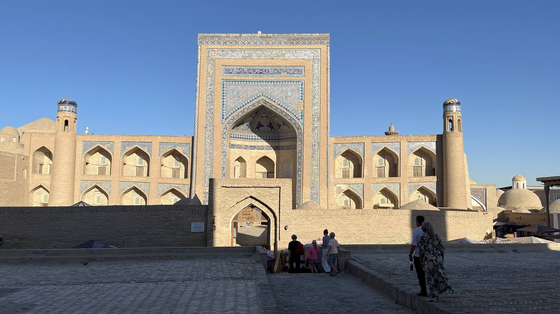Madrasa a Khiva con maioliche blu, turisti seduti all'ombra