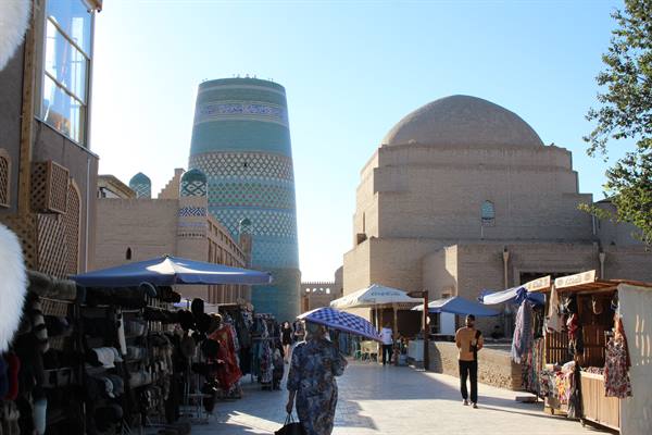 Khiva: minareto maiolato e mercato sotto ombrelloni a mezzogiorno