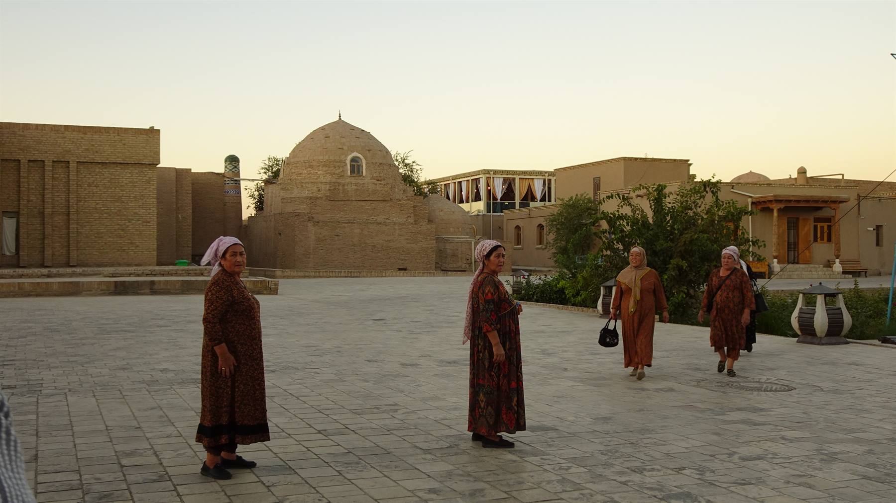 Donne in veste tradizionale camminano su lastre davanti alla madrasa di Khiva