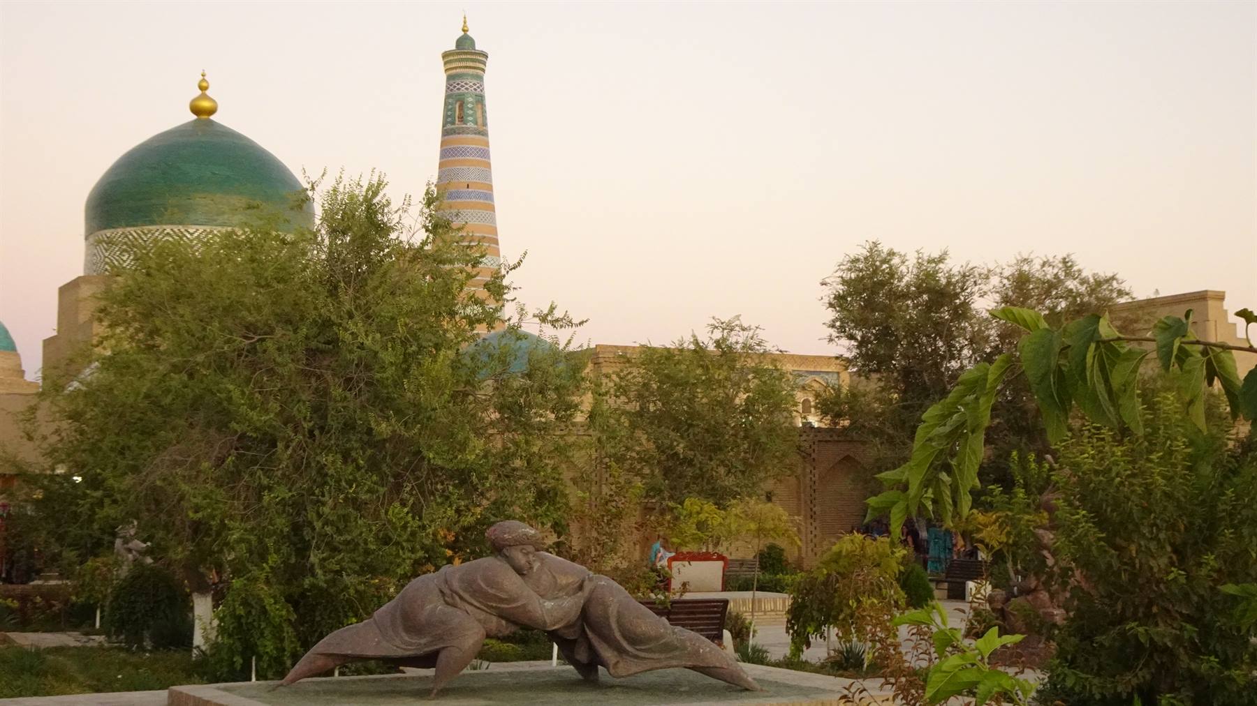 Khiva: statua di lottatori davanti al minoreto Islam Khoja al crepuscolo