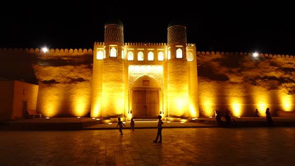 Mura illuminate di notte a Khiva, bambini che corrono nella piazza