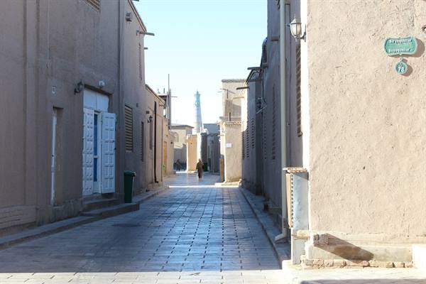 Vicolo lastricato tra muri di argilla con minareto sullo sfondo, Khiva