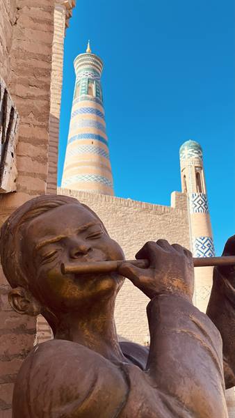 Statua di bronzo di un fanciullo flautista sotto i minareti di Khiva