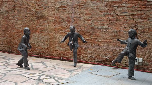 Bronze statues of children playing against a red brick wall