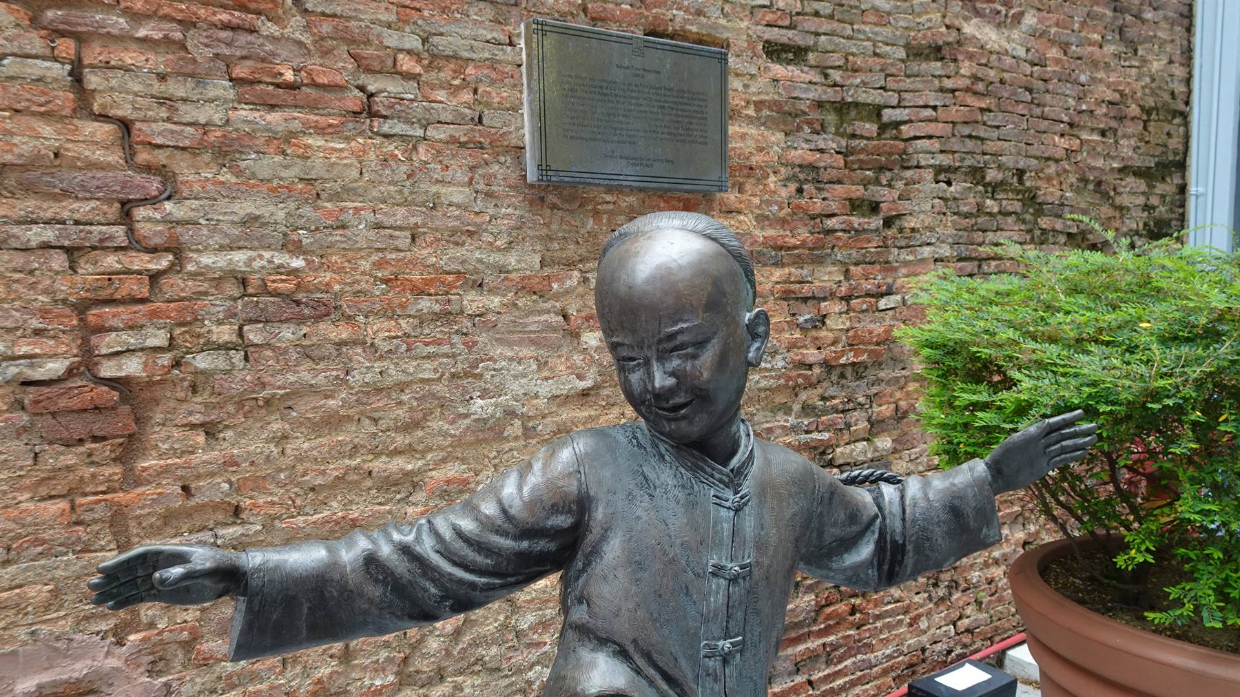 Un bambino di bronzo danza felice tra mattoni antichi e verde.