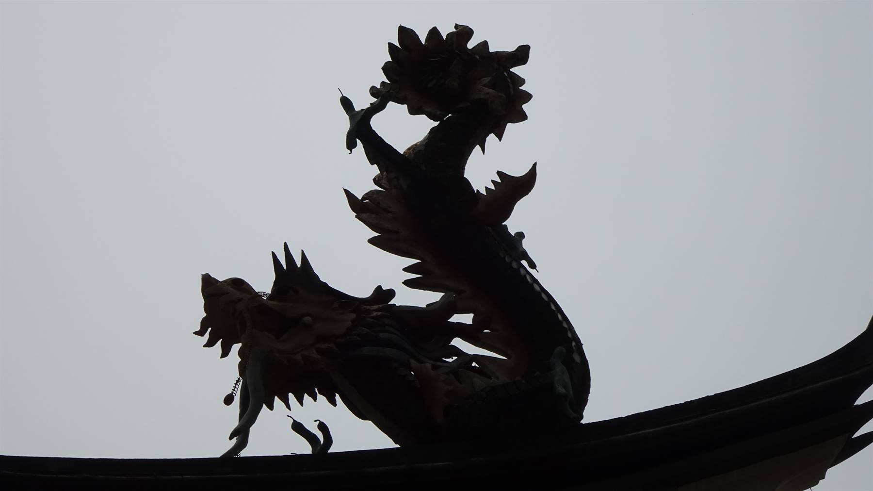 Statua di drago in silhouette sul tetto curvo di un tempio, cielo grigio