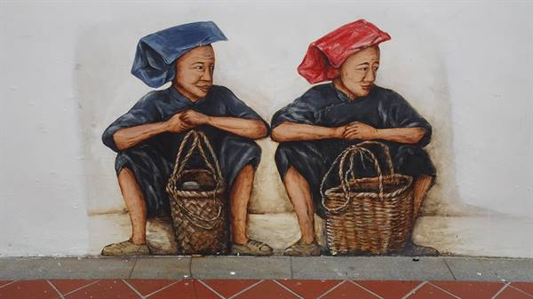 Mural of two seated women with woven baskets, blue and red headscarves, on white wall