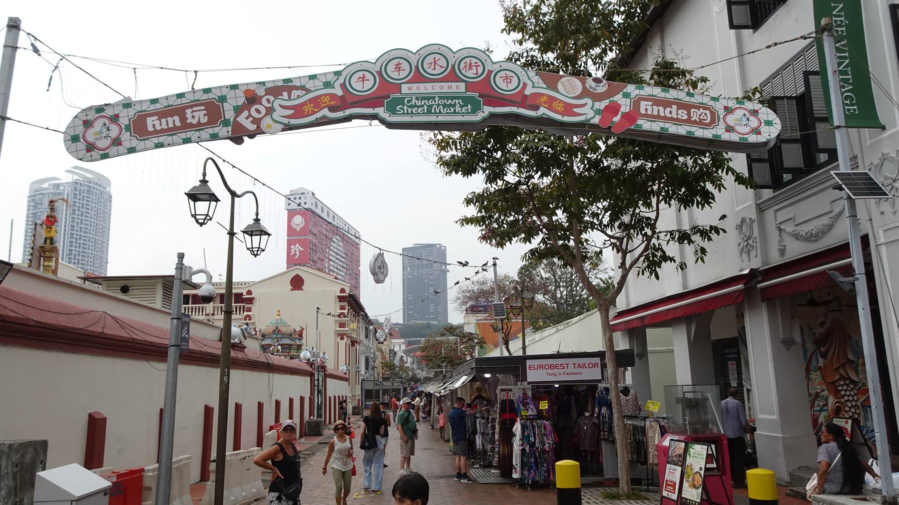 Insegna di Chinatown Street Market sopra la strada affollata, turisti tra i banchi, grattacieli sullo sfondo