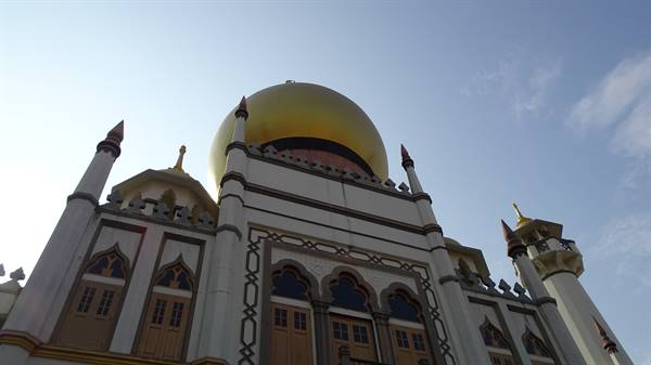 Golden dome of Sultan Mosque in Singapore among white spires under blue sky