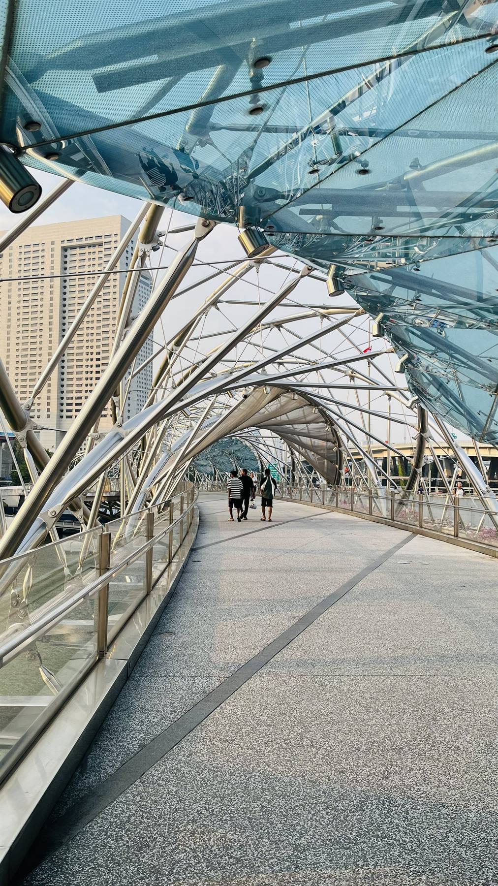 Passeggeri camminano sull'Helix Bridge di Singapore tra strutture in acciaio e vetro