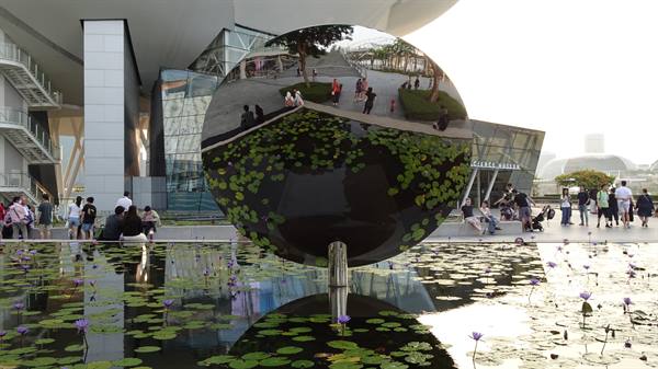 Mirror sphere reflecting the ArtScience Museum and visitors among water lilies