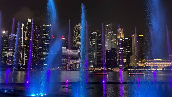 Blue and purple illuminated water jets at Marina Bay among night skyscrapers