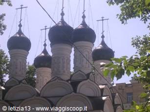 Black onion domes of an Orthodox church framed by green leaves, Moscow