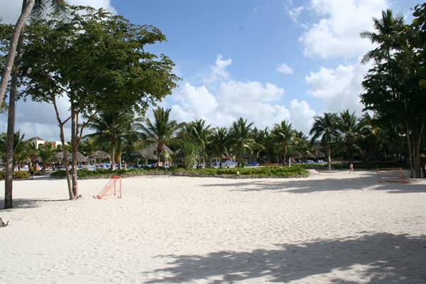 White sand beach with palm trees, thatched umbrellas and small volleyball goals