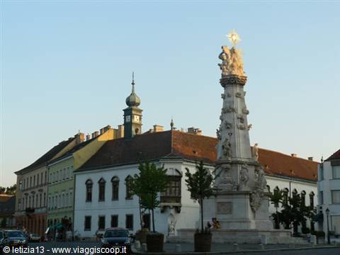 Baroque marble plague column on a square, church tower behind, Győr