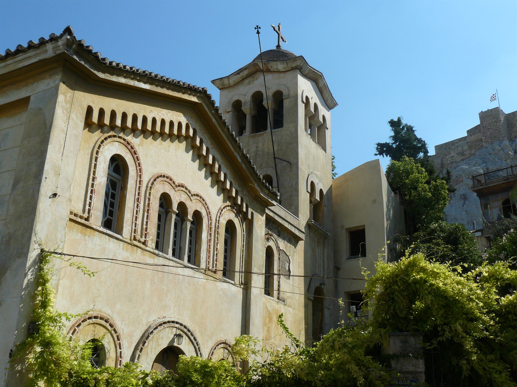 Chiesa bizantina in pietra con campanile e bifore, verde rampicante, sotto cielo azzurro