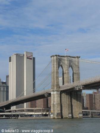 Brooklyn Bridge stone towers with American flag, skyscrapers and the East River