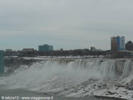 Frozen Niagara Falls under grey sky, skyscrapers along the shore