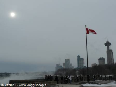 Tourists beneath the Canadian flag, Skylon Tower rising over Niagara Falls mist