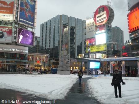 Snow-covered Dundas Square in Toronto, glowing billboards and bundled-up pedestrians